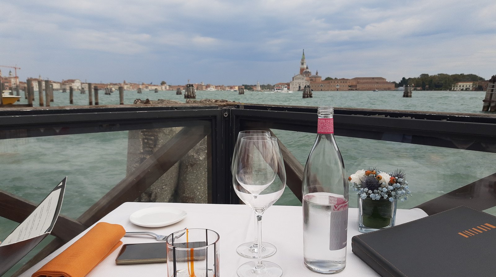 A table set with linen and glassware on a terrace over the water.