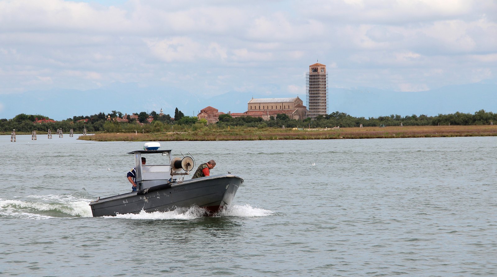 Fishermen navigating a boat off the shore of Torcello island.