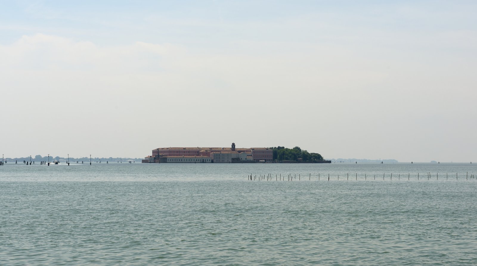 San Clemente island seen across the water, its former monastery buildings among trees.