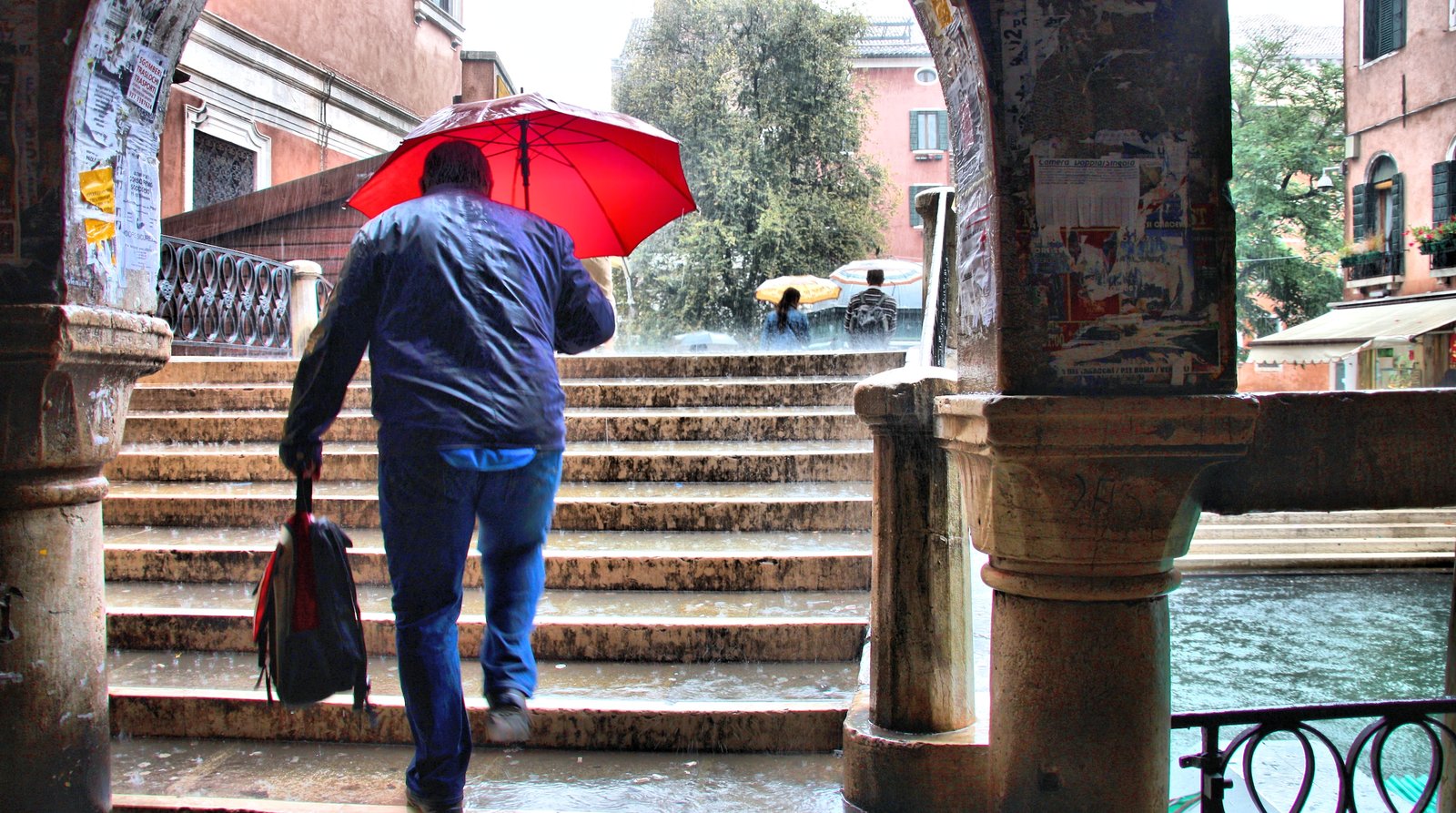 Pedestrians crossing a Venice bridge in the rain.