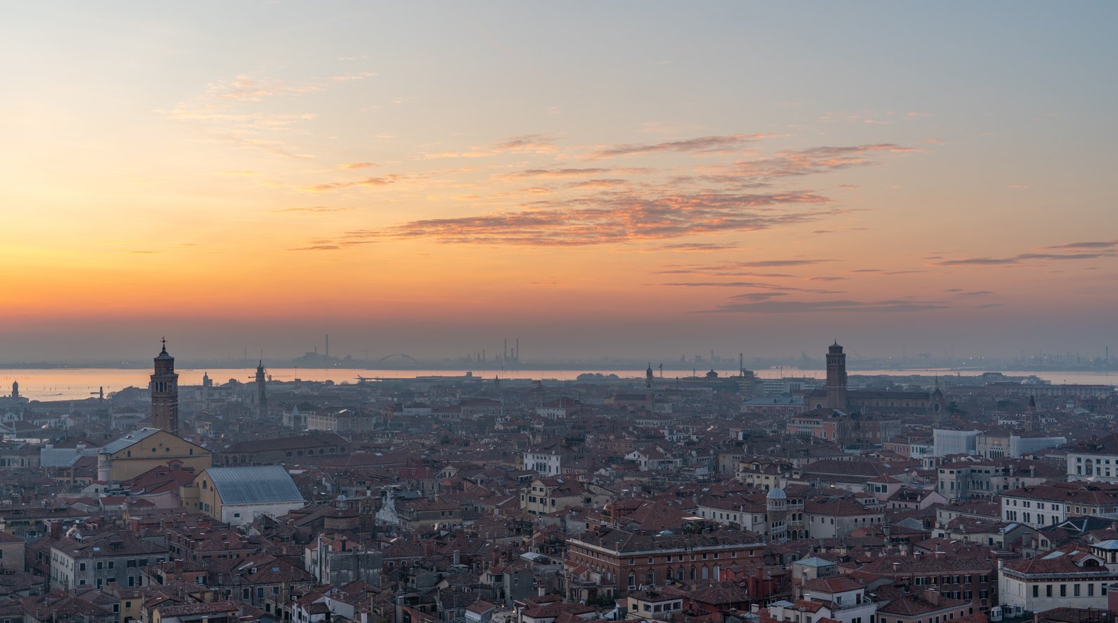 An aerial view of Venice's rooftops stretching toward the lagoon at sunset.