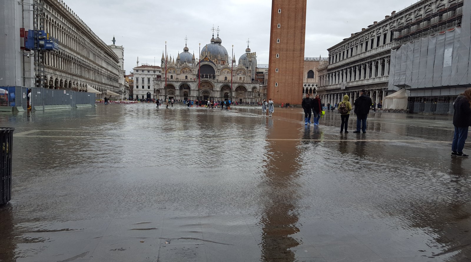 Acqua alta flooding across Piazza San Marco, with visitors crossing on raised walkways.