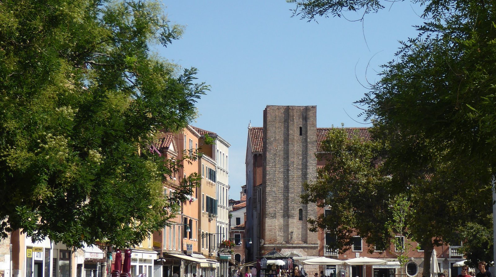 Residents crossing a Venetian campo lined with shops and stalls.